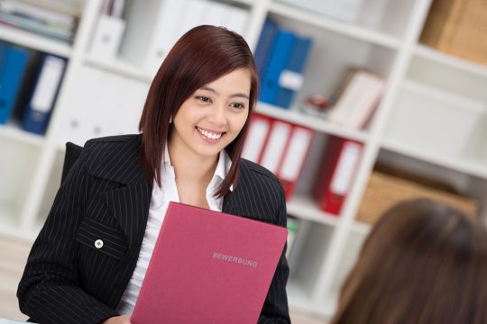 4_Executive-Coaching-for-Career-Transitions 26571207 - smiling young asian woman in a job interview sitting talking to the employment officer with her curriculum vitae in her hands
